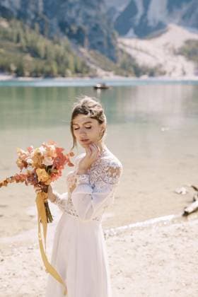 Schöne Braut in einem weißen Kleid mit Ärmeln und Spitze, mit einem gelben Herbststrauß aus Trockenblumen und Pfingstrosen, am Pragser Wildsee in Italien. Destination Hochzeit in Europa, am Pragser Wildsee Beautiful bride in a white dress with sleeves and lace, with a yellow autumn bouquet of dried flowers and peony roses, on the Lago di Braies in Italy. Destination wedding in Europe, on Braies lake Copyright: imageBROKER NadtochiyxVladimir ibxiqx13170972.jpg ,model released, Symbolfoto ,property released