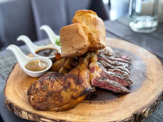 A succulent plate of steak slices and roasted chicken leg served with Yorkshire pudding and a trio of delicious sauces, presented on a rustic wooden board on a cafe in Thailand Model Released IrinaChetverikova_ID28328_834977_006 Copyright: xIrinaxChetverikovax