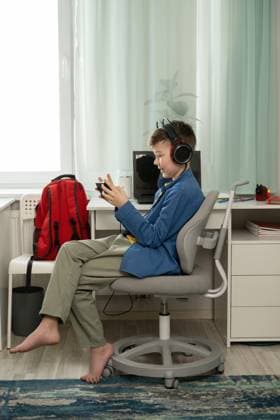 IMAGO Creative, Lifestyle, Gaming MR_ID28313_20909_IgorSushin.jpg, PR_ID28313_10984_Room.jpg, MR_ID28313_20910_AnnaSushina.jpg A young boy sits barefoot, focused on his mobile game. Wearing headphones, he enjoys gaming in his comfortable room with a backpack nearby and a tidy desk, Property released Model Released LiliyaSolopova_ID28313_834569_036 Copyright: xLiliyaxSolopovax