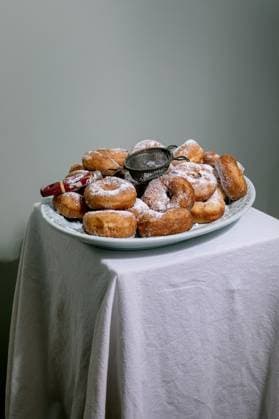 Selbstgemachte Donuts mit Puderzucker Fresh homemade donuts dusted with powdered sugar served on blue plate with sifter. Traditional sweet pastry breakfast dessert against minimal background. (License=RF) Copyright: xZoonar.com NATASHAxBREENx 23381697