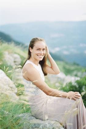 Creative Highlight Symbolbilder Ein lächelndes Mädchen glättet ihr Haar mit der Hand, während sie auf einem Stein in den Bergen sitzt Smiling girl straightens her hair with her hand while sitting on a stone in the mountains. Copyright: imageBROKER VolodymyrxNadtochii ibxiqx13181026.jpg ,model released, Symbolfoto ,property released