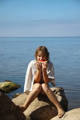 Creative Highlight Symbolbilder A girl sits on a stone in the summer and eats a watermelon. Saint Petersburg, Saint Petersburg, Russia CR_JLUFVV250512-1726458-01 ,model released, Symbolfoto