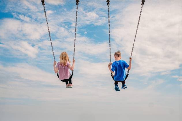 Creative Highlight Symbolbilder Two children swinging high under a blue, cloud-filled sky. Marblehead, Massachusetts, United States CR_MJOR250513-1726277-01 ,model released, Symbolfoto