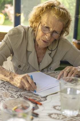 Ältere Frau mit Brille, die an einem Tisch mit einem Glas Wasser mit Buntstiften auf einem Notizbuch zeichnet und eine entspannende und kreative Tätigkeit in ihrem Ruhestand genießt Senior woman with glasses drawing with crayons on a notebook at a table with a glass of water, enjoying a relaxing and creative activity in her retirement Copyright: imageBROKER MariaxDanielaxRomero ibxktg13422585.jpg ,model released, Symbolfoto ,property released