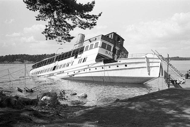 Die S S Saxaren kentert und sinkt im Mai 1964 an der Anlegestelle Stor Krans im westlichen Saxarfjärden. Das Schiff gilt als Wrack und wird 1973 von der Reederei Strömma erworben, wo es unter seinem ursprünglichen Namen S S Gustafsberg VII restauriert wird. Auf dem Bild ist das Schiff bei der Hafeneinfahrt zu sehen The S S Saxaren capsizes and sinks at Stor-Krans jetty in western Saxarfjärden in May 1964. The vessel is deemed a wreck and, in 1973, is acquired by the Strömma shipping company, where it is restored to its original name, S S Gustafsberg VII. Pictured when it seen listing to port Copyright: imageBROKER Sjoberg ibljsj13777538.jpg