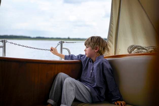Creative Highlights Symbolbilder A young boy in casual wear sits on a boat, gazing at the water under a cloudy sky. Mecklenburg Lake Plateau, Mecklenburg-Western Pomerania, Germany Mecklenburg-Western Pomerania Germany bola08459 Copyright: xConnectxImagesx ,model released