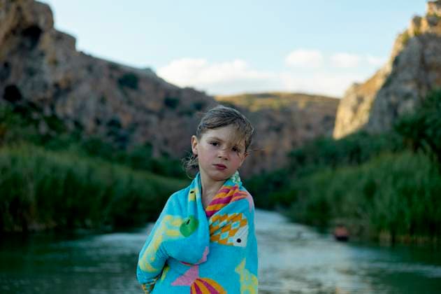 Creative Highlights Symbolbilder Child wrapped in a colorful towel stands by a serene river with rocky cliffs in the background. Crete, Greece bola08466 Copyright: xConnectxImagesx ,model released