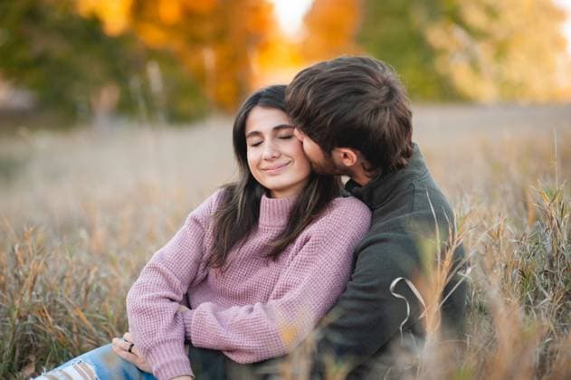 Young couple kissing cheek sitting down in pretty autumn field Grimes, Iowa, United States CR_LIPF250524-1737273-01 ,model released, Symbolfoto