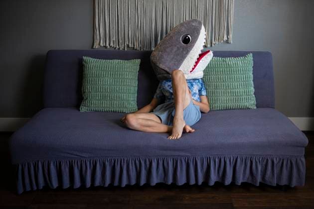 Creative Highlights Symbolbilder Child in shark head costume lounging on blue couch Norman, Oklahoma, United States R_AOVS250524-1736565-01 ,model released, Symbolfoto