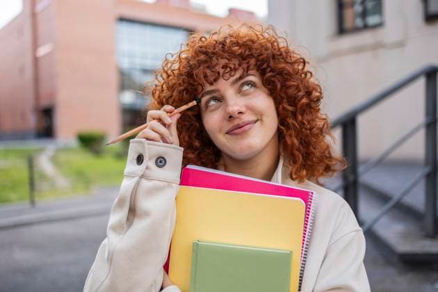 Creative Highlights Symbolbilder Student with curly red hair holding notebooks and a pencil, smiling outdoors at a university campus model released, Symbolfoto, JCCMF13415