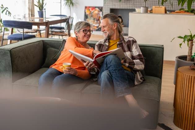Senior couple enjoying a catalog on the sofa in their living room model released, Symbolfoto property released, JCCMF13563