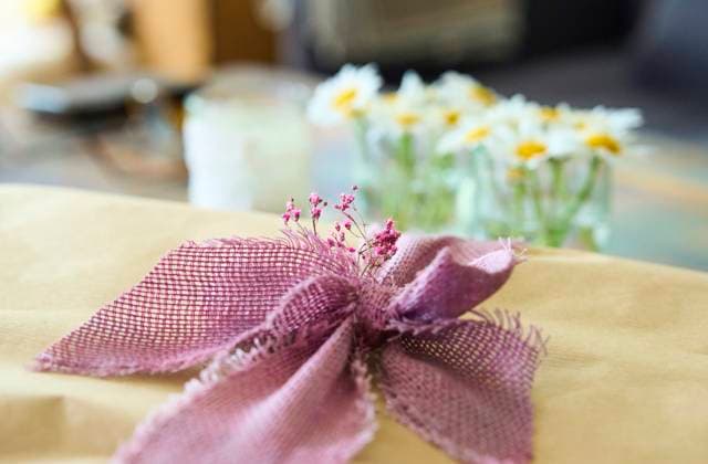A beautifully wrapped gift adorned with a purple ribbon and small pink flowers on May 27, 2025 in Marktoberdorf, Germany,