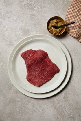A fresh piece of beef steak displayed on a white ceramic plate, accompanied by grainy mustard in a small dish. Perfect for culinary and butcher themes, showcasing high-quality meat preparation. Model Released GeorgiaGold_ID28577_843651_042 Copyright: xGeorgiaxGoldx