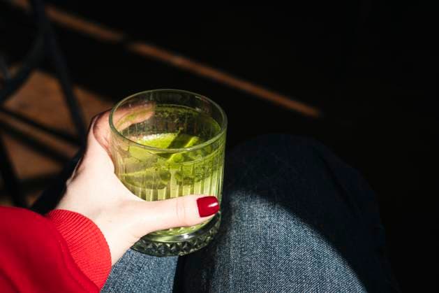 Cropped unrecognizable woman in red holding a glass of matcha tea, with a moody lit background emphasizing the vibrant green of the drink. Model Released HannaYakimenko_ID28426_837042_009 Copyright: xHannaxYakimenkox