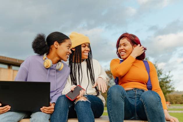 Three latin women sitting outdoors on a campus, engaging in lively conversation and sharing laughs, with laptops and smartphones, showcasing a moment of friendship and relaxation Model Released AlbertoMenendez_ID15110_461119_043 Copyright: xAlbertoxMenendezx RECORD DATE NOT STATED