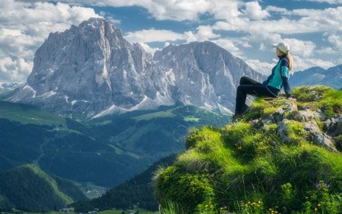Sitting girl on the top with yellow flowers and green grass in beautiful alpine mountain valley at sunset in summer. Landscape with relaxing woman in alps, sky with clouds, rocks. Dolomites, Italy Model Released DenisBilytskyi_ID26964_778294_015 Copyright: xDenisxBilytskyix