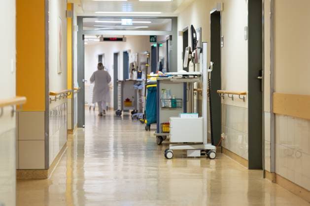 Deutschland 25. April 2025: Im Bild: Dieses Foto zeigt einen langen, sauberen und hellen Krankenhausflur, der einen realistischen Einblick in den Alltag einer modernen medizinischen Einrichtung bietet. Der glänzende Boden reflektiert das Licht, was auf hohe Hygienestandards und eine regelmäßige Reinigung schließen lässt. Entlang des Ganges sind an beiden Seiten Handläufe aus hellem Holz angebracht, die Patienten und Besuchern Unterstützung bieten. Mehrere medizinische Rollwagen und Gerätschaften sind strategisch platziert, darunter im rechten Vordergrund ein mobiler medizinischer Wagen mit einem Monitor und anderen Instrumenten, bereit für den Patienteneinsatz. Im Hintergrund ist eine Person in medizinischer Kleidung, wahrscheinli Copyright: xFotostandx xGelhotx