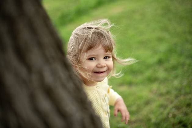 Creative Highlights Symbolfotos Cute little blond European girl peeking out from behind a tree. Corby, England, United Kingdom R_JNDO250523-1735662-01 ,model released, Symbolfoto