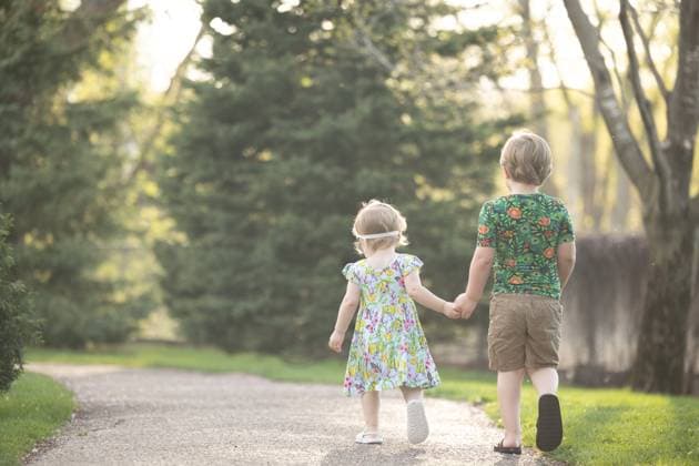 IMAGO Creative, Ostern, Bräuche, Osterspaziergang #2 Two children holding hands walking on sunlit garden path Bloomington, Minnesota, United States R_DMBV250605B-1739516-01 ,model released, Symbolfoto