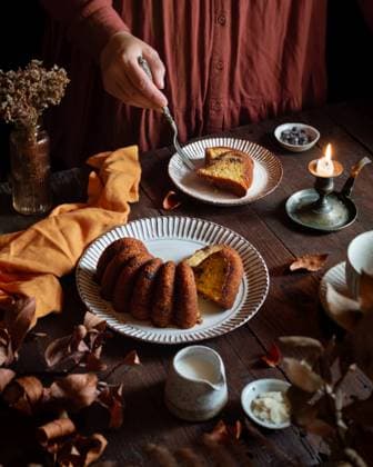 A cozy scene featuring a homemade pumpkin cake on a wooden table. Warm lighting highlights the cake™s texture, with fall decor adding to the autumnal ambiance Model Released EvelynPernas_ID28724_848613_002 Copyright: xEvelynxPernasx
