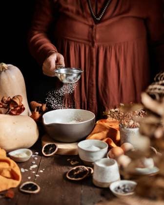 A cozy autumn scene of a homemade pumpkin cake being prepared. A person sprinkles ingredients into a bowl surrounded by pumpkins, spices, eggs, and dried fruits Model Released EvelynPernas_ID28724_848614_003 Copyright: xEvelynxPernasx