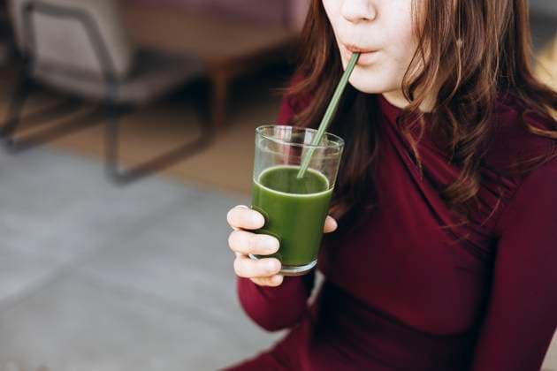 Creative Highlights Symbolfotos A young female student enjoys a healthy green smoothie through a straw, sitting in a cozy room. She is wearing a burgundy top, savoring the refreshing drink with focus Model Released HannaYakimenko_ID28947_860557_027 Copyright: xHannaxYakimenkox
