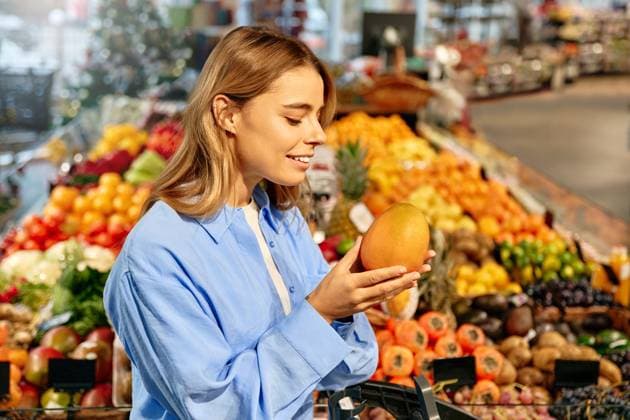 Woman enjoying the scent of ripe mango at fruit market Young woman smiling while holding and smelling a ripe mango in a vibrant supermarket produce section. Concept of healthy lifestyle, fresh tropical fruits, and sensory enjoyment of food. Model Released OrionProduction_ID29903_1009870_074 Copyright: xTonyBeardyx