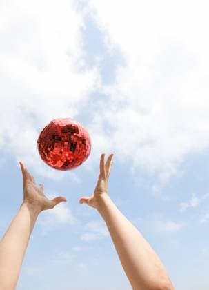 Creative Highlights Symbolbilder Hands tossing large red disco ball into a blue cloudy summer sky New York, New York, United States R_UTHC250611-1766400-01 ,model released, Symbolfoto