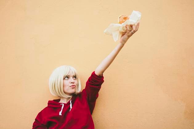 Creative Highlights Symbolbilder Woman holding hamburger with hand raised in front of peach wall model released, Symbolfoto, SVCF00206