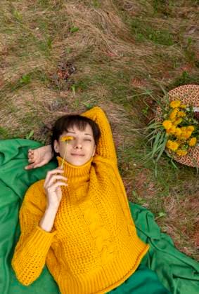Creative Highlights Symbolbilder Smiling woman lying on a grassy field with a flower before her eyes and a hat with dandelions model released, Symbolfoto, MBLF00856