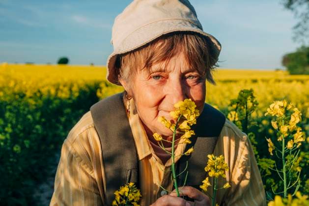Creative Highlights Symbolbilder Senior woman enjoying a spring day in a rapeseed field while backpacking model released, Symbolfoto, VSNF03309