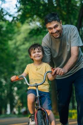 Father teaching son to ride a bicycle outdoors in summer model released, Symbolfoto, ANAF04778