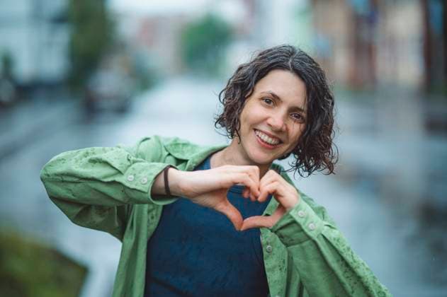 Smiling woman making heart symbol in city on rainy day model released, Symbolfoto, ANAF04798