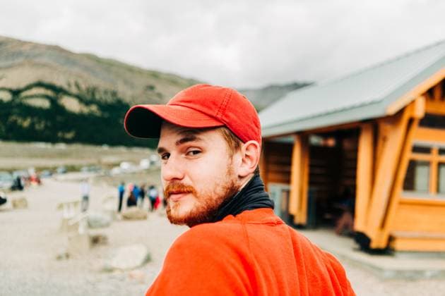 Creative Highlights Symbolbilder Man in red hat and shirt looks back near lodge in mountain setting. Jasper, Alberta, Canada CR_XPQF250623C-1735351-01 ,model released, Symbolfoto