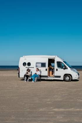 Entspannen am Strand in Dänemark mit einem Wohnmobil an einem sonnigen Tag A couple enjoys a peaceful day at a beach in Denmark, lounging outside their camper van. The clear blue sky enhances their relaxing atmosphere as they savor the tranquil surroundings. (License=RF) ,model released, Symbolfoto Copyright: xZoonar.com FokkexBaarssenx 23681347 ,model released, Symbolfoto ,property released