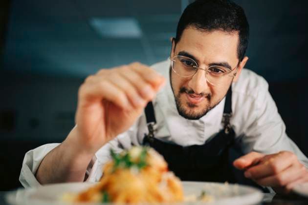 Creative Highlights Symbolbilder Smiling male chef sprinkling grated cheese on tagliatelle pasta in kitchen at restaurant Sweden, Gothenburg, model released, property released Copyright: xMaskotx , MA117948 MA117948