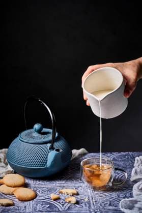 Creative Highlights Symbolbilder A calming scene with milk being poured into tea from a white jug, surrounded by a traditional teapot and milk cookies on a patterned table. The setup offers a warm, inviting atmosphere Model Released AnaGomez_ID28946_860378_004 Copyright: xAnaxGomezx RECORD DATE NOT STATED