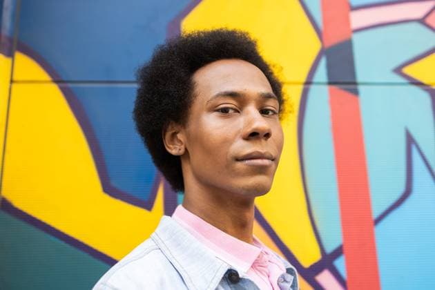 Creative Highlights Symbolbilder MR_ID29905_21601_BrianRijo.jpg A non-binary person with an afro hairstyle gazes confidently at the camera, standing against a vibrant, geometric mural. The image captures a blend of cultures and expressions Model Released DavidMunoz_ID29905_1010051_026 Copyright: xDavidxMunozx RECORD DATE NOT STATED