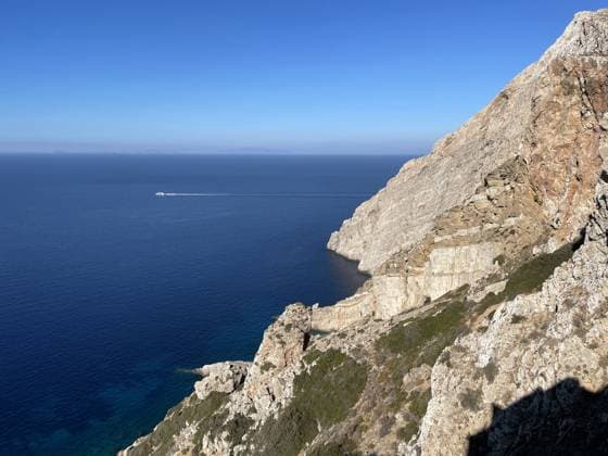 Tiefblaues Ägäisches Meer mit einer Klippe A cliff arises from the calm blue sea on the Aegean coast of the island of Folegandros. A boat is speeding off in the distance. (License=RF) Copyright: xZoonar.com HermelinkxKerstinx 23653029