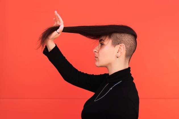 Creative Highlights Symbolbilder A young woman with a modern undercut hairstyle poses against a vibrant red background. Her stylish look is complemented by ear piercings and a black turtleneck. Model Released Jultud_ID29095_888544_001 Copyright: xJultudx
