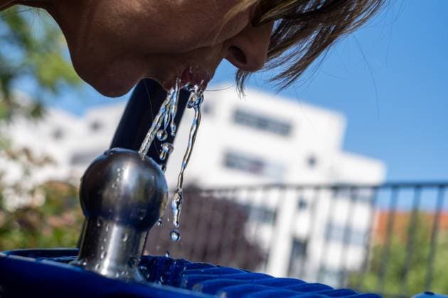 Junge Frau trinkt Wasser aus einem Berliner Trinkbrunnen. Young woman drinking water from a Berlin drinking fountain. Hitzewelle in Berlin