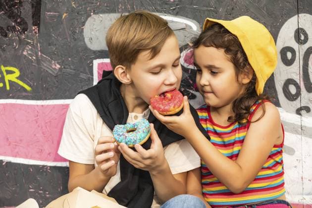 Kinder essen bunte, süße und leckere Donuts. Kinder knabbern an ungesunden Lebensmitteln im Freien. Lebensmittellieferung oder Essen zum Mitnehmen Konzept Kids eating colorful sweet and tasty donuts. Children snacking on unhealthy food outdoors. Food delivery or take away food concept Copyright: imageBROKER ZulfiiaxIshmukhameto ibxiqx14289732.jpg ,model released, Symbolfoto ,property released