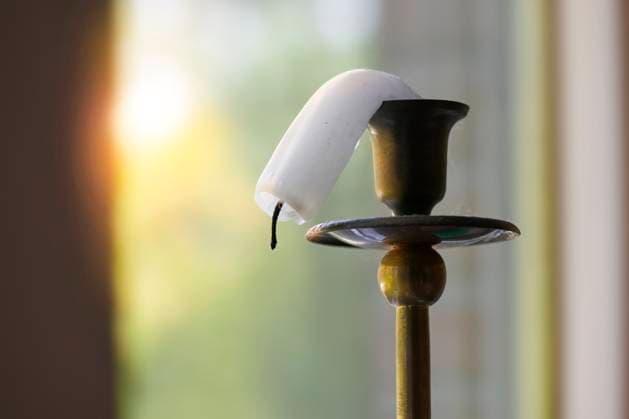 Symbolbild Klima, eine Kerze auf einem Messingständer schmilzt in der Hitze am Fenster und biegt sich nach unten Sommerhitze