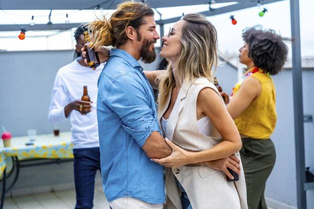 Ein glückliches Paar, das sich umarmt und freudige Momente mit Freunden teilt, während es auf einer lebhaften Dachparty unter den Lichtern der Stadt Getränke schlürft Happy couple embracing and sharing joyful moments with friends while sipping drinks at a lively rooftop party under the city lights Copyright: imageBROKER UnaixHuizi ibxuhu14211878.jpg ,model released, Symbolfoto ,property released