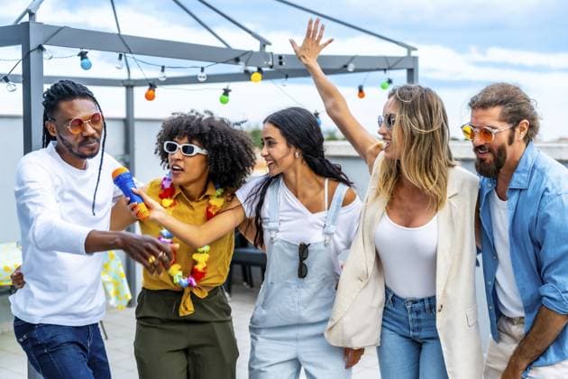 Eine Gruppe verschiedener Freunde feiert auf einem Dach, singt Karaoke, tanzt fröhlich und genießt gemeinsam eine ausgelassene Sommerparty Group of diverse friends celebrating on a rooftop, singing karaoke, dancing joyfully, and enjoying a vibrant summer party together Copyright: imageBROKER UnaixHuizi ibxuhu14211891.jpg ,model released, Symbolfoto ,property released