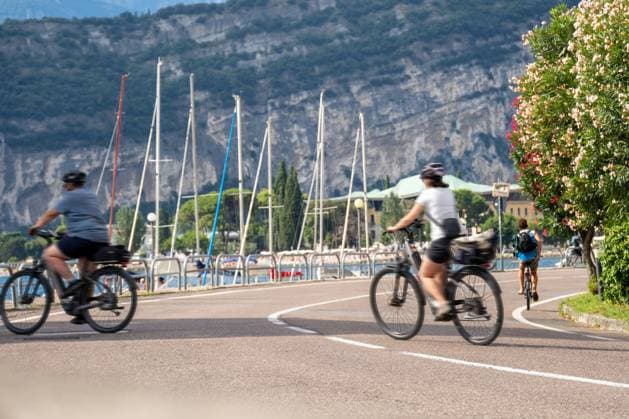Torbole, Lake Garda, Italy - July 15, 2025: Cyclists on the promenade on Lake Garda - on the move with helmet and luggage along the lakeside road, where lake and mountains offer an active vacation route. *** Radfahrerinnen und Radfahrer auf der Promenade am Gardasee unterwegs mit Helm und Gepäck entlang der Uferstraße, wo See und Berge eine aktive Urlaubsstrecke bieten.