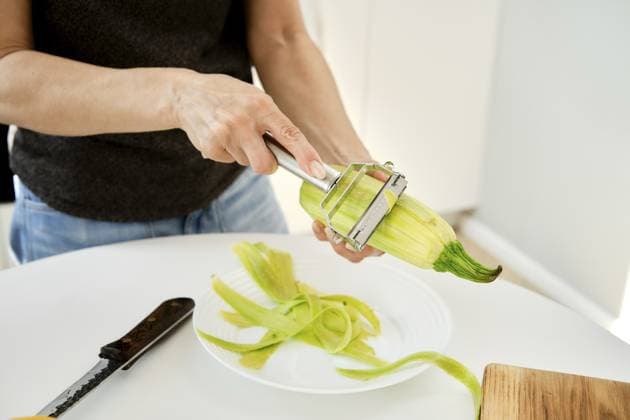 Eine Person schält eine Zucchini in einer hellen Küche. Frische Zucchini werden in einer Hand gehalten, während ein Schäler die Schale entfernt A person is peeling a zucchini in a bright kitchen. Fresh zucchini is held in one hand while a peeler removes the skin Copyright: imageBROKER AlekseixIsachenko ibxfbm14362542.jpg ,model released, Symbolfoto ,property released