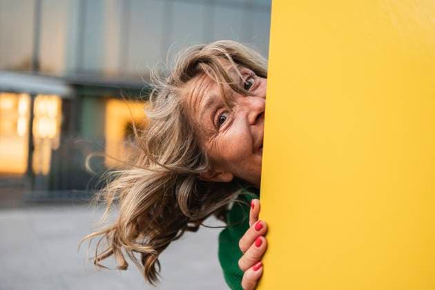 Creative Highlight Symbolbilder Playful mature woman peeking from behind yellow panel outdoors model released, Symbolfoto, JCCMF13823