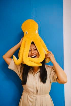 Creative Highlight Symbolbilder Smiling woman posing with octopus toy on head against blue background model released, Symbolfoto property released, AMWF03577