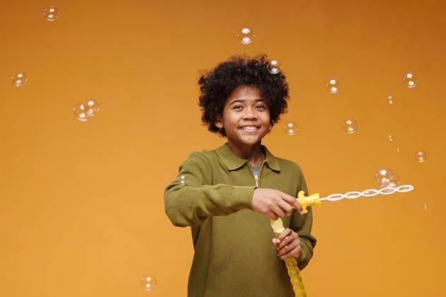 Creative Highlight Symbolbilder Smiling kid playing with soap bubbles indoors against yellow background model released, Symbolfoto, DSHF02534